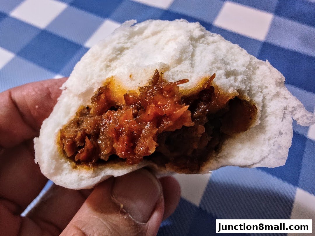 A close-up shot of a person holding a steamed bun filled with savory meat.