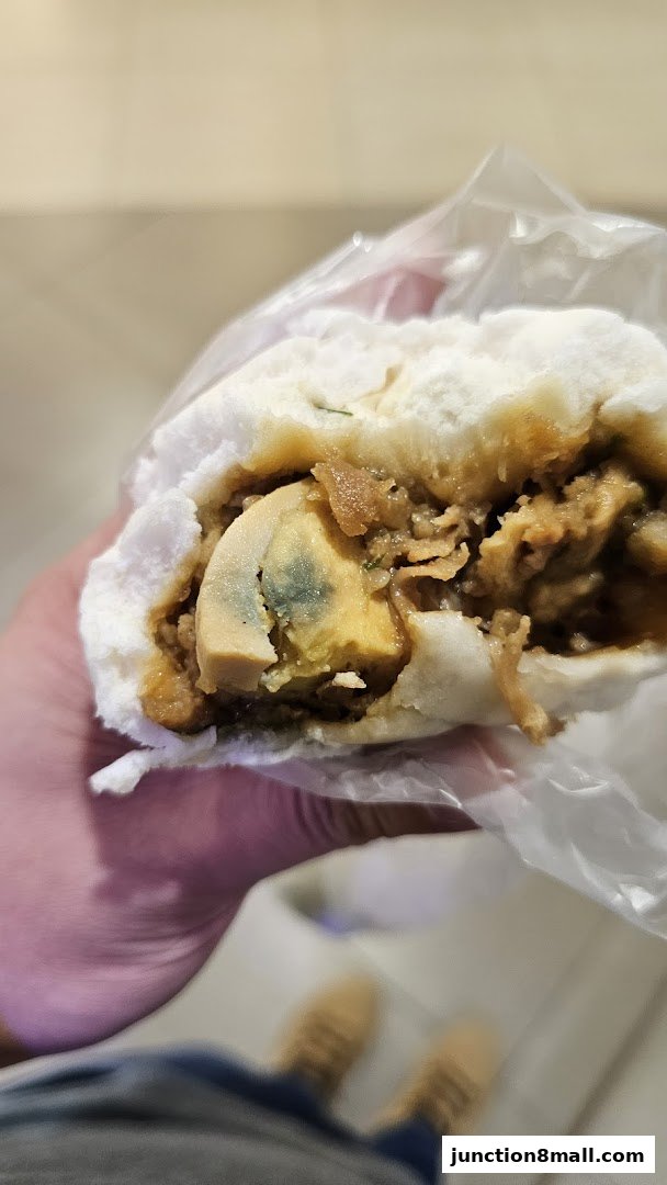 A close-up shot of a person holding a steamed bun filled with savory ingredients and a preserved egg.