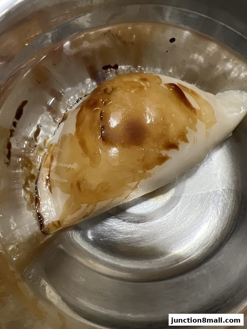 A close-up shot of a steamed bun drizzled with sauce in a metal bowl.