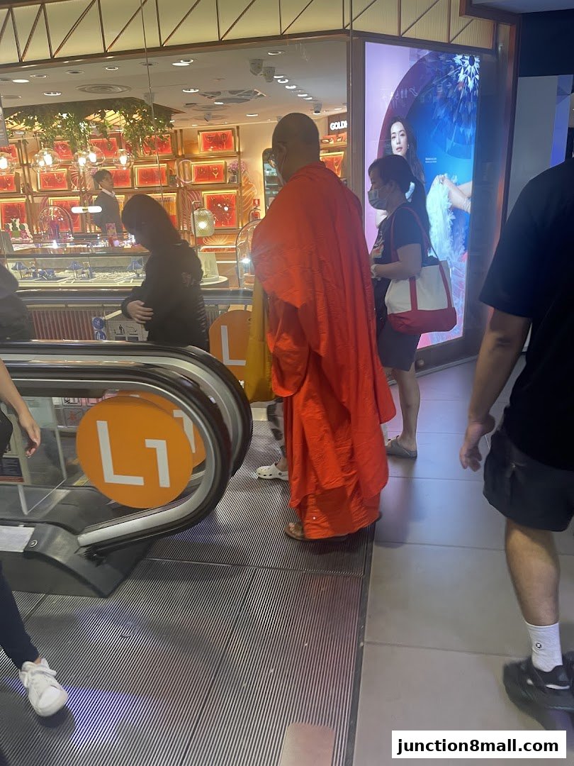 People on an escalator in front of a jewelry store with a large advertisement.