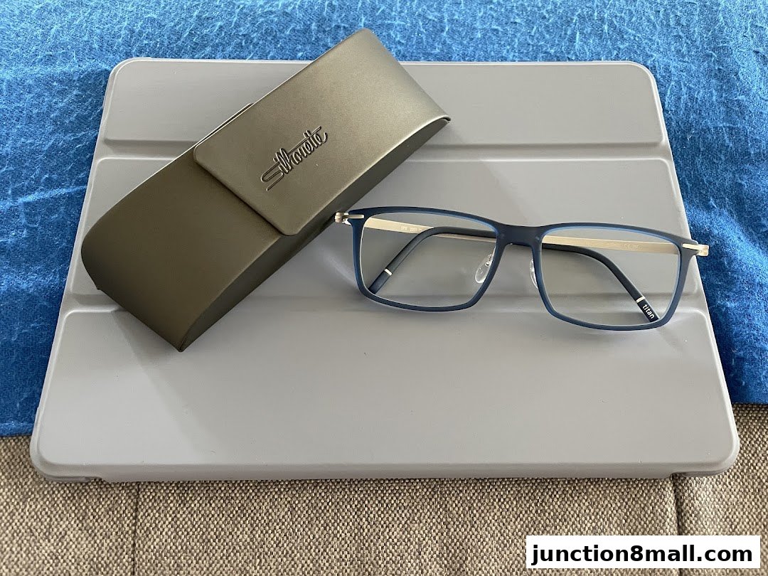 A pair of blue and gold rimmed glasses with a Silhouette case on a gray surface.
