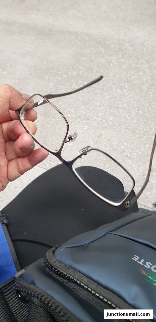 A hand holds a pair of eyeglasses with a dark frame and clear lenses.