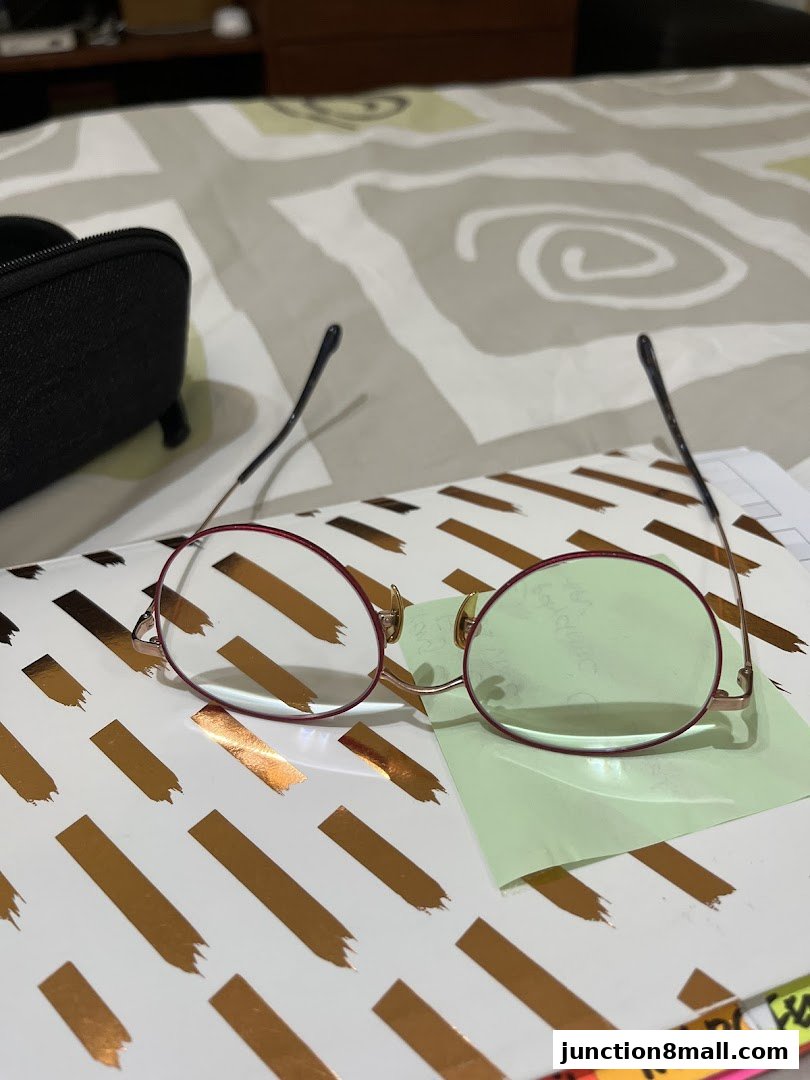 A pair of red-rimmed eyeglasses with a glasses case on a patterned surface.
