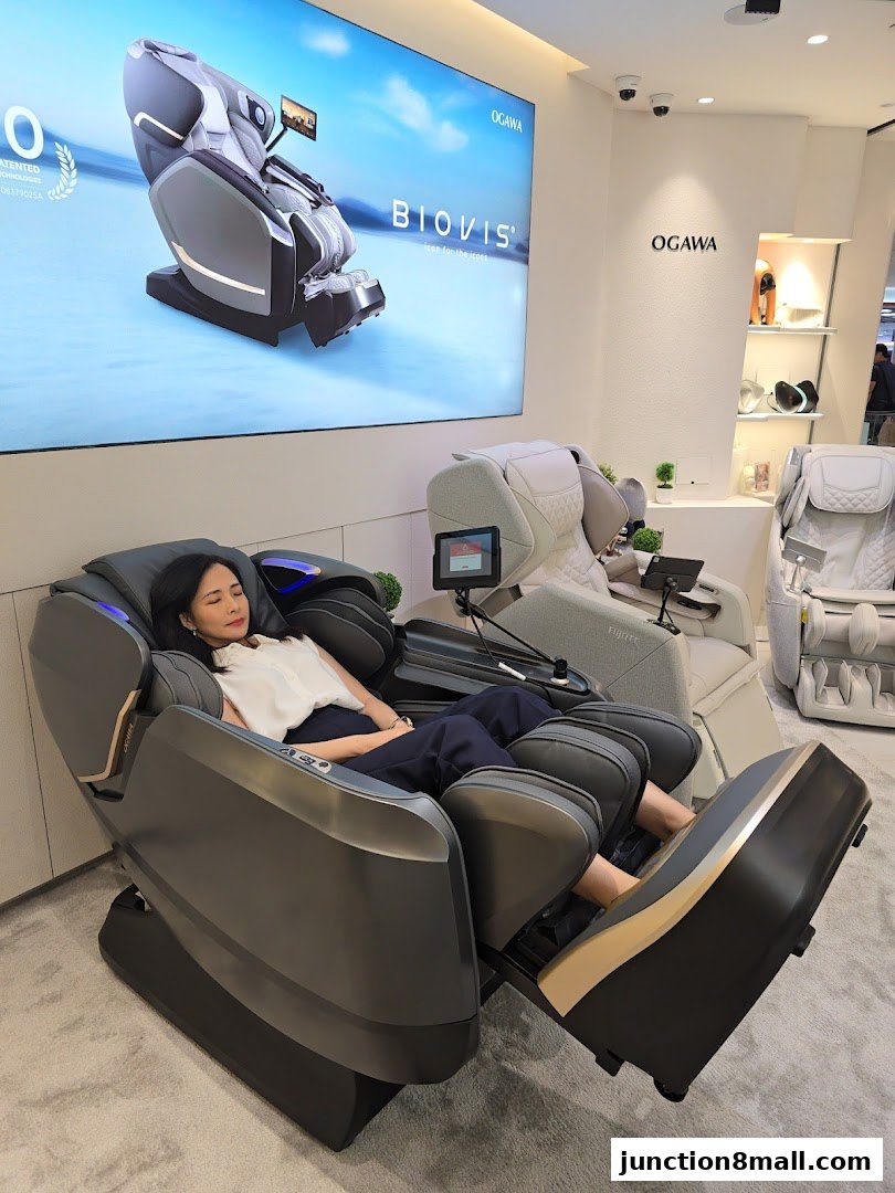 A woman relaxes in a massage chair at the OGAWA store, with a large screen displaying a massage chair.