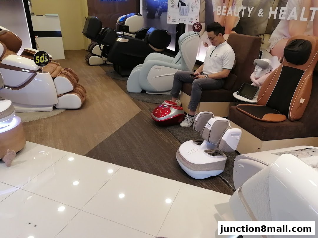 A man sits in a massage chair while various massage chairs and foot massagers are displayed.