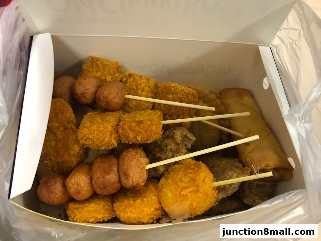 A box filled with various fried snacks on skewers, including sausages and spring rolls.