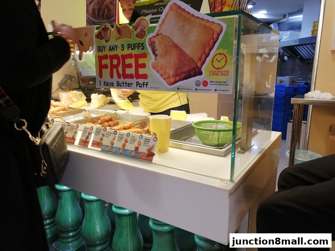 A display counter at Old Chang Kee showcasing various fried snacks and a promotion for free puffs.