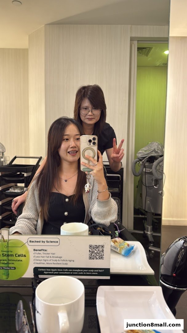 Two women smiling at the camera in a hair salon, one taking a selfie.