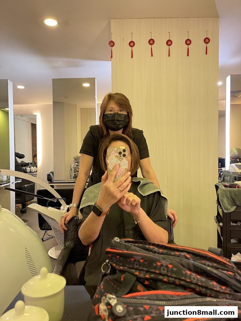 A hairstylist stands behind a client who is taking a selfie in a salon.