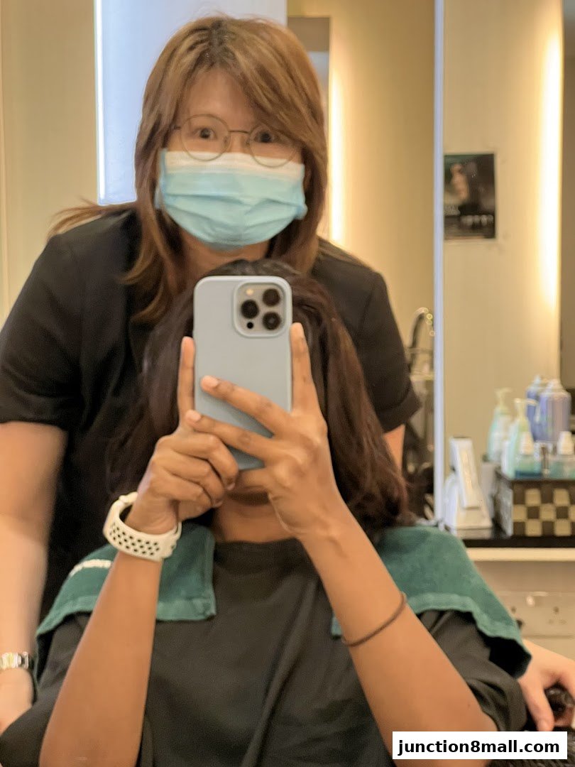 A hairstylist wearing a mask takes a selfie with a client in a salon.