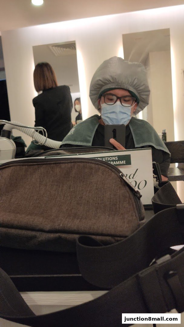 A person wearing a hair cap and mask takes a selfie in a salon.