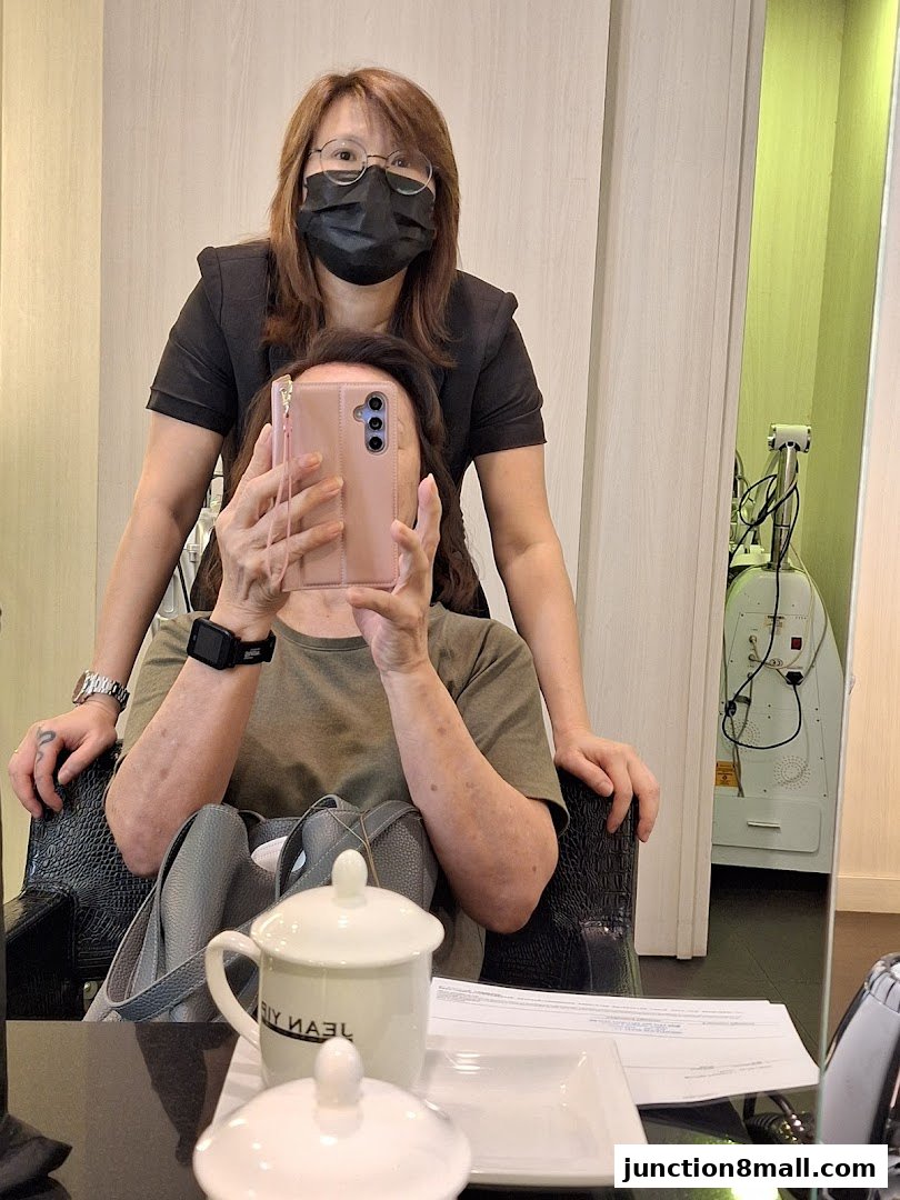 Two women in a salon, one taking a selfie with a phone, the other standing behind.