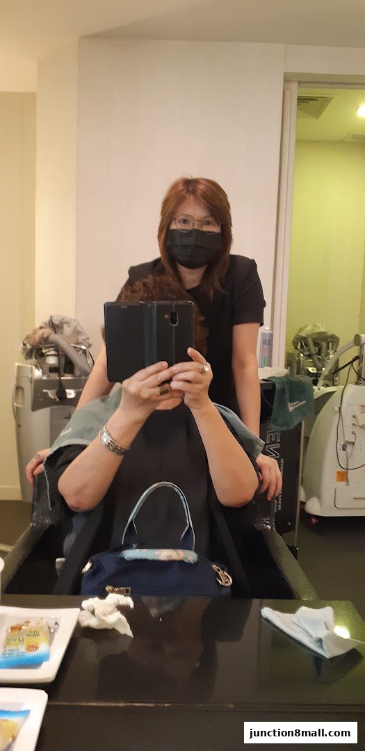 A hairstylist in a mask stands behind a client in a salon chair, taking a mirror selfie.