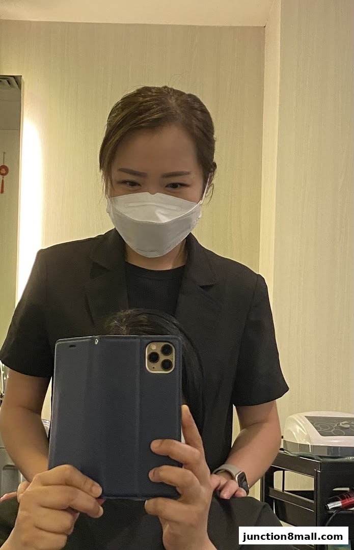 A woman wearing a mask and a black blazer takes a selfie in a salon.