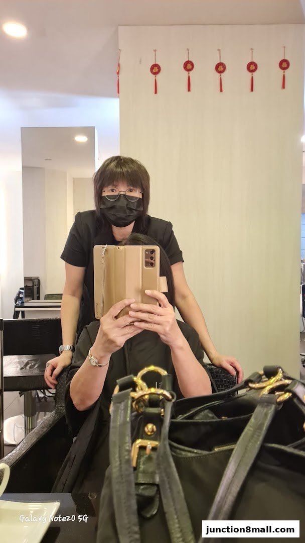 A hairstylist in a mask stands behind a client taking a mirror selfie.