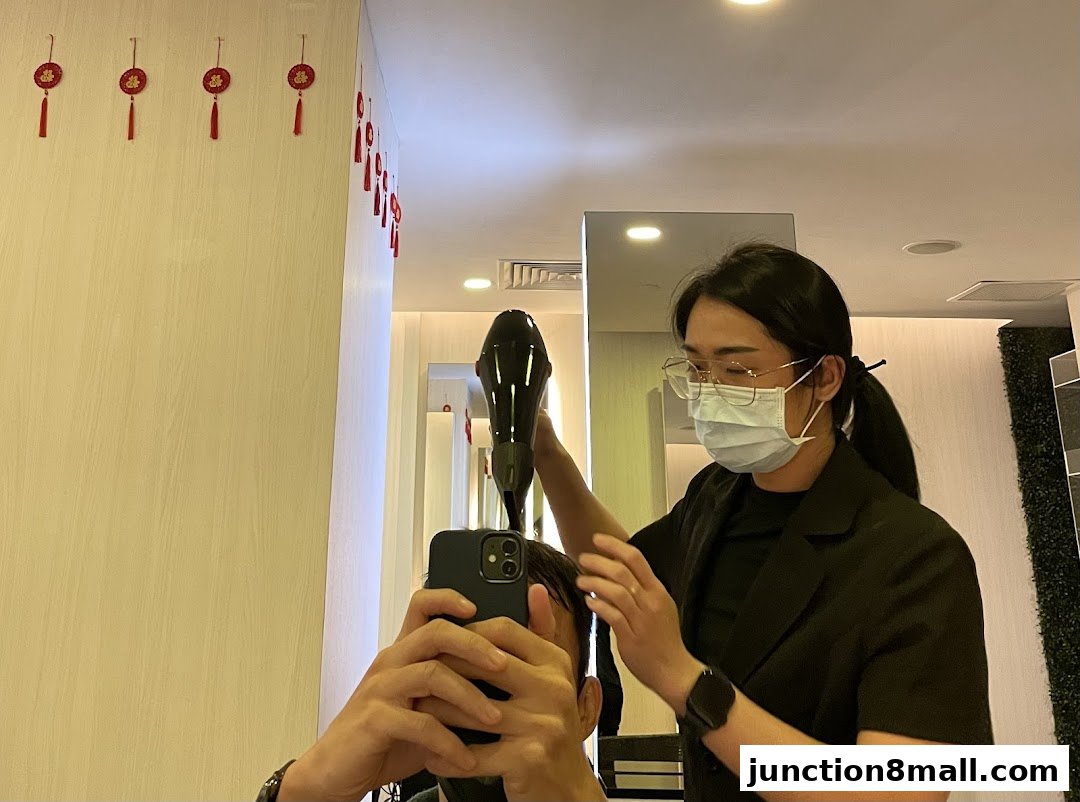 A hairstylist blow-drying a client's hair while the client takes a selfie.