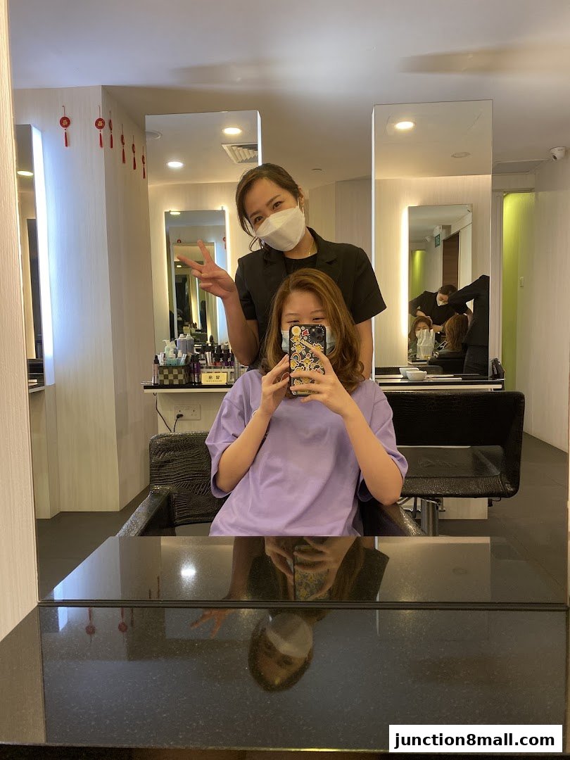 A hairstylist poses with a client in a salon, both wearing masks.