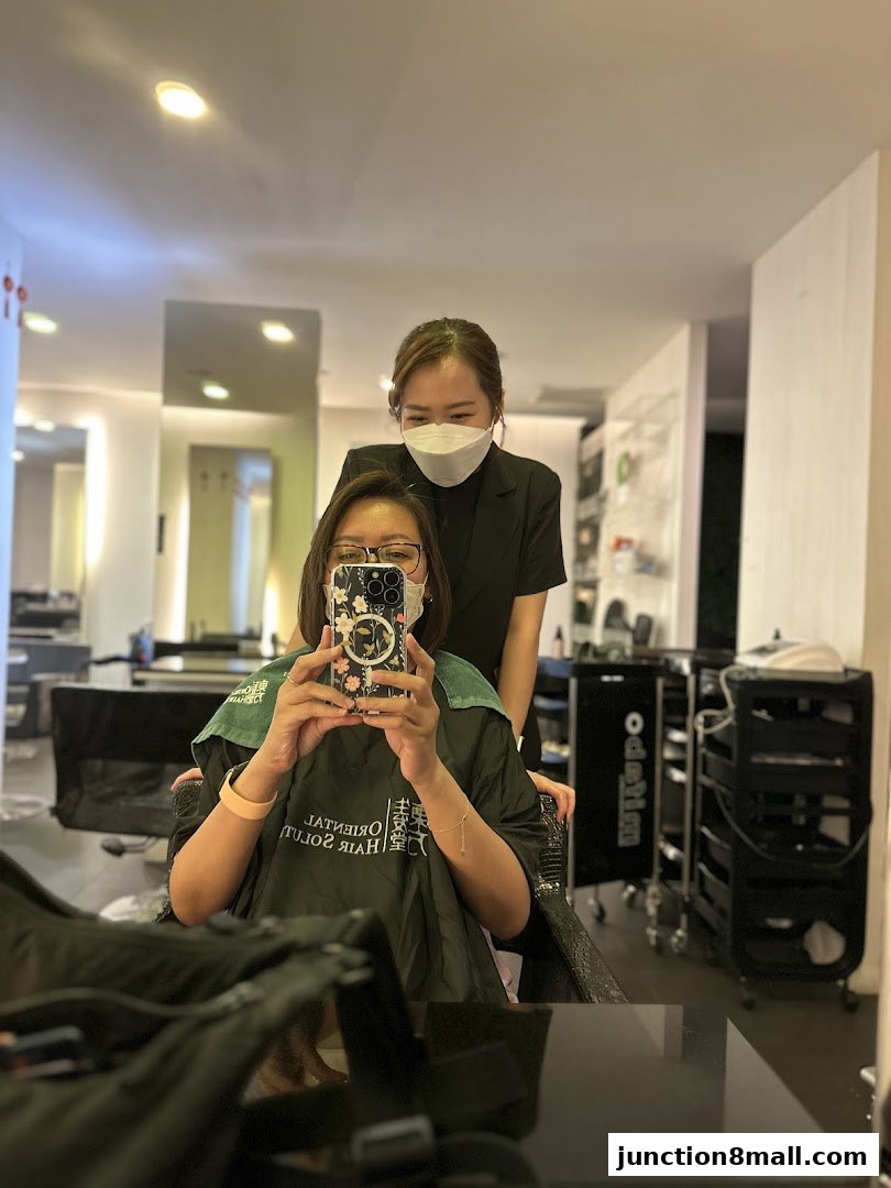 A person in a salon chair takes a selfie with a stylist behind them.