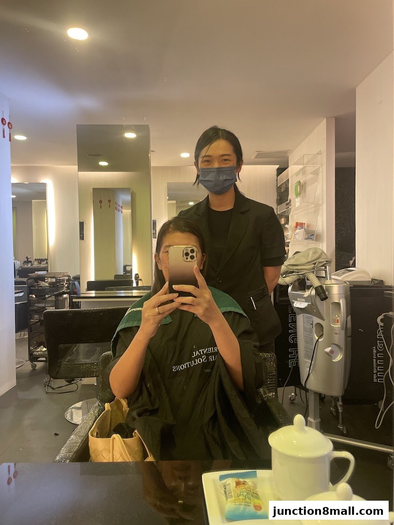 A person in a salon cape takes a selfie with a stylist behind them.