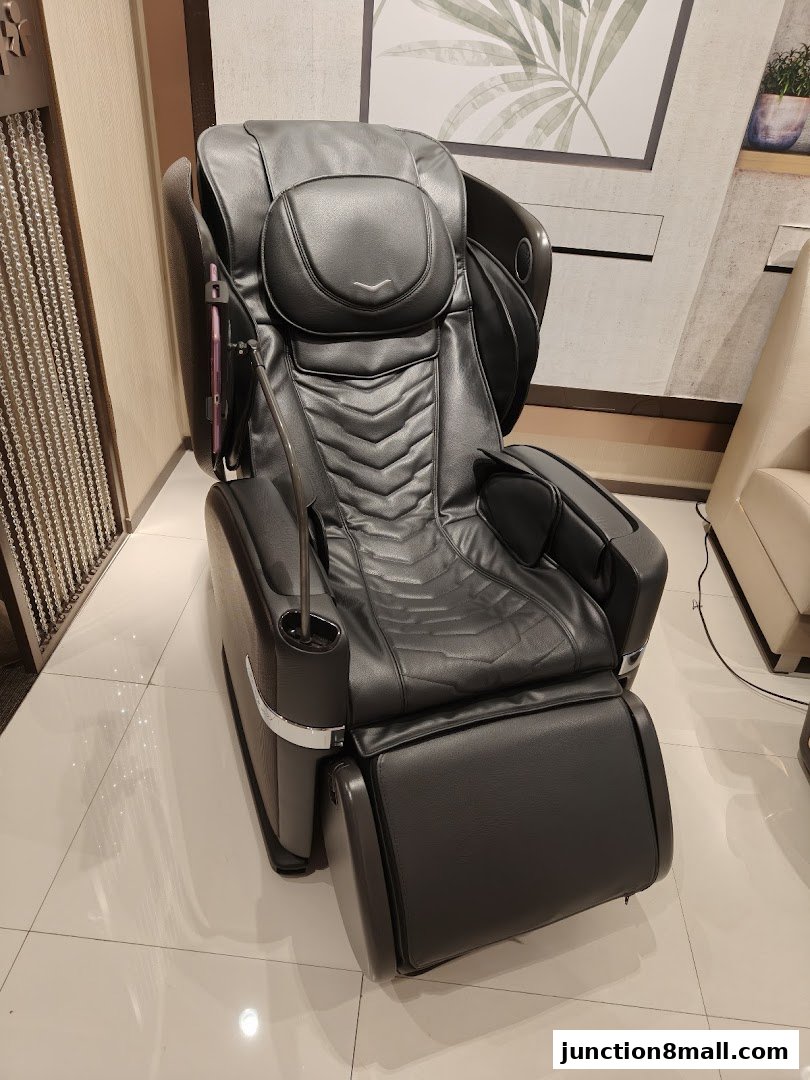 A luxurious black massage chair with a footrest is displayed in a well-lit retail space.