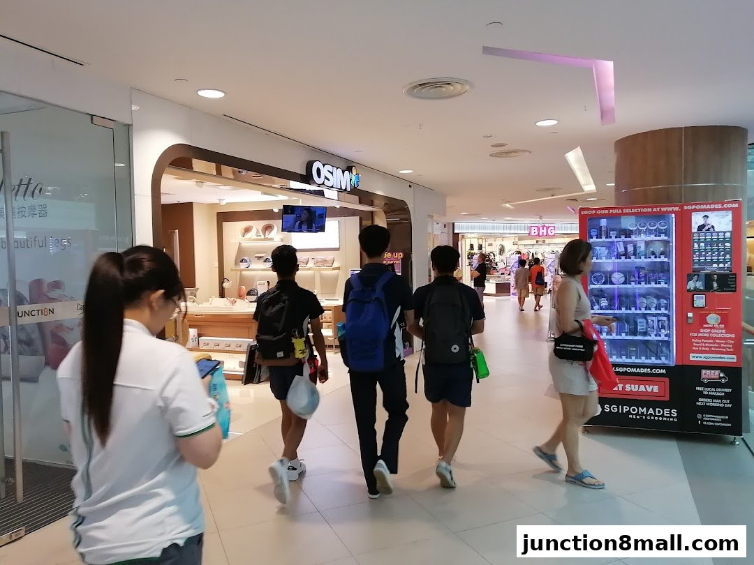 People walking past an OSIM store and a grooming product vending machine in a mall.
