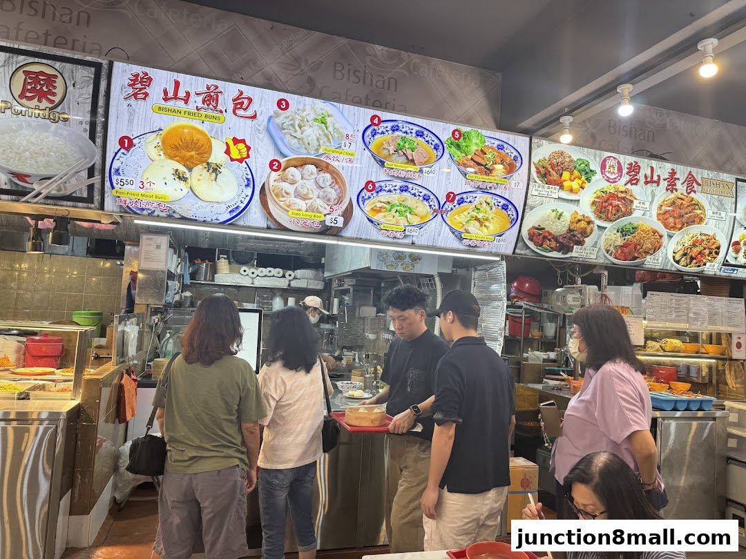 A busy food stall with a menu board displaying various dishes and customers ordering.
