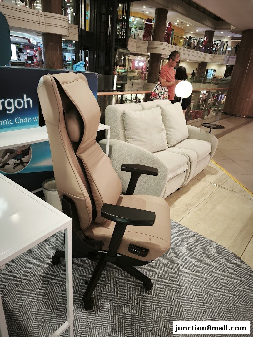 A beige massage chair and a sofa are displayed in a shopping mall.