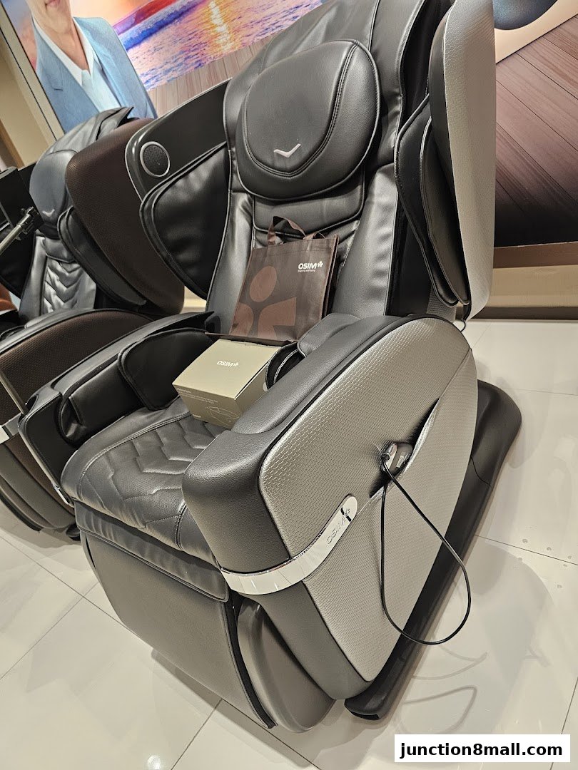 A close-up view of a luxurious OSIM massage chair with a branded shopping bag and box.