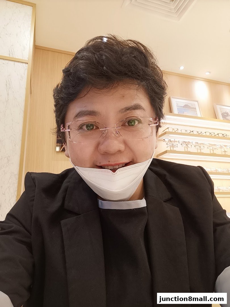 A person wearing glasses and a mask smiles in an optical shop with displays of eyewear.