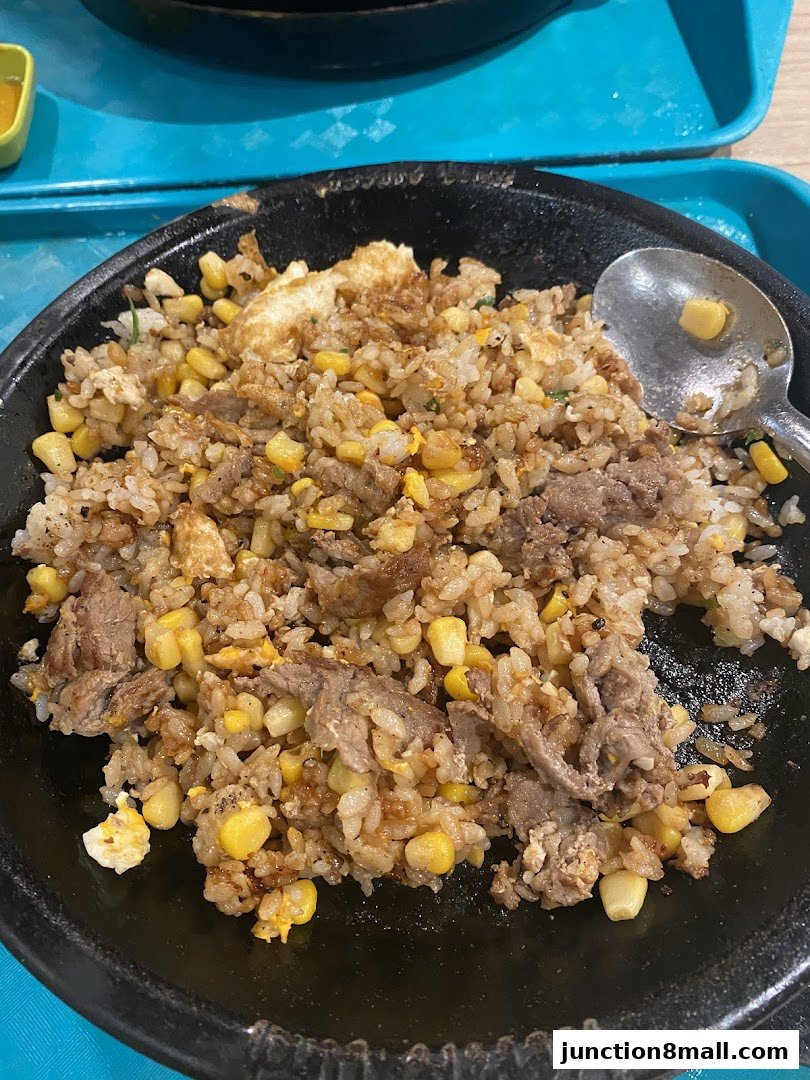 A sizzling plate of beef and corn fried rice with a spoon.