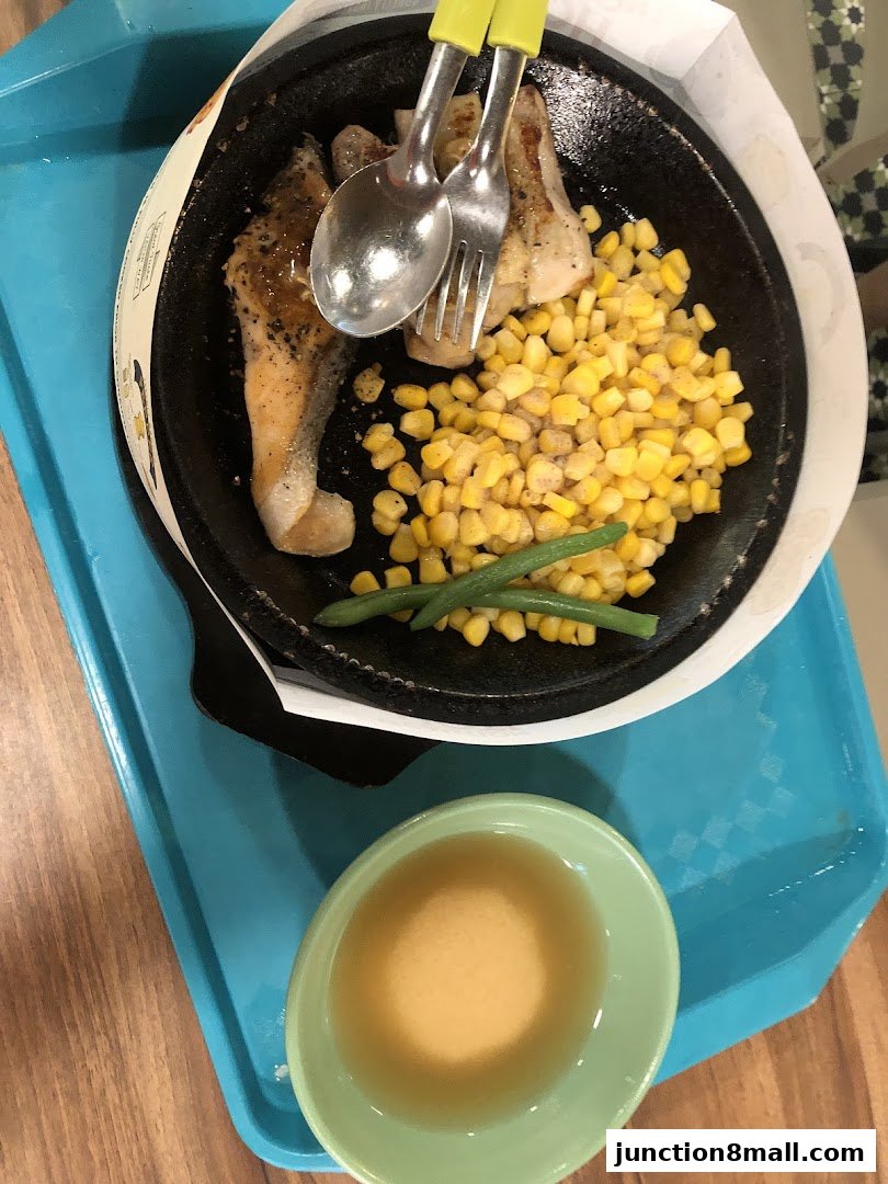A sizzling plate of salmon with corn and green beans, served with a side of sauce.
