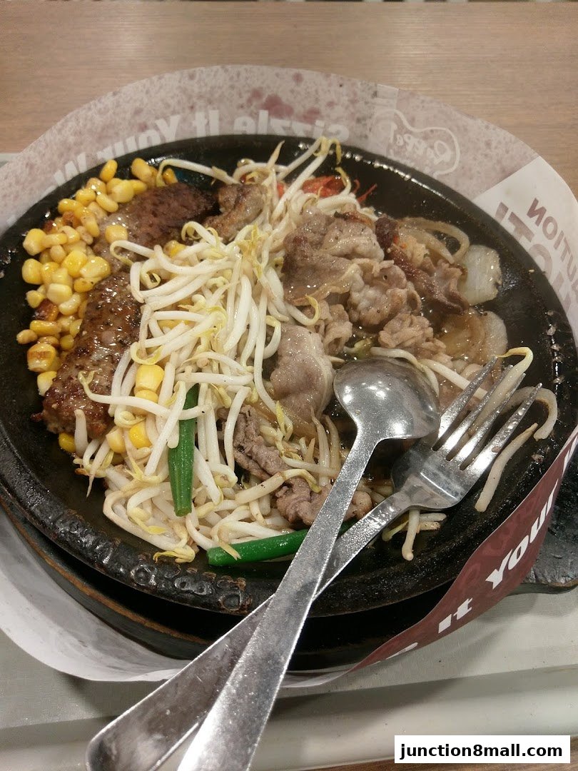 A sizzling hot plate of beef, corn, and bean sprouts with cutlery.
