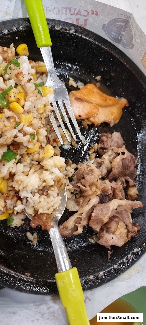A sizzling hot plate meal with rice, corn, chicken, and beef, served with cutlery.