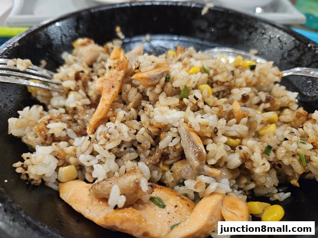 A close-up shot of a sizzling plate of salmon fried rice with corn and spring onions.