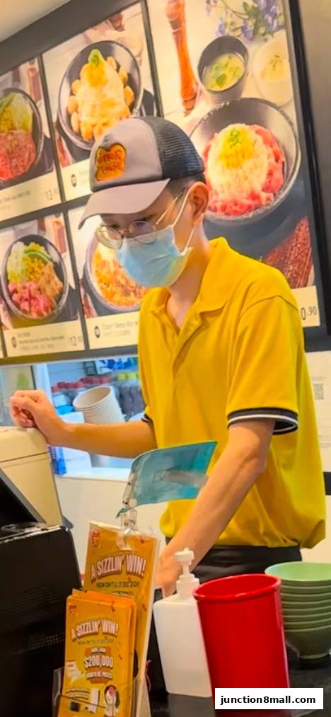 A staff member in a yellow shirt stands at a counter with food displays and promotional materials.
