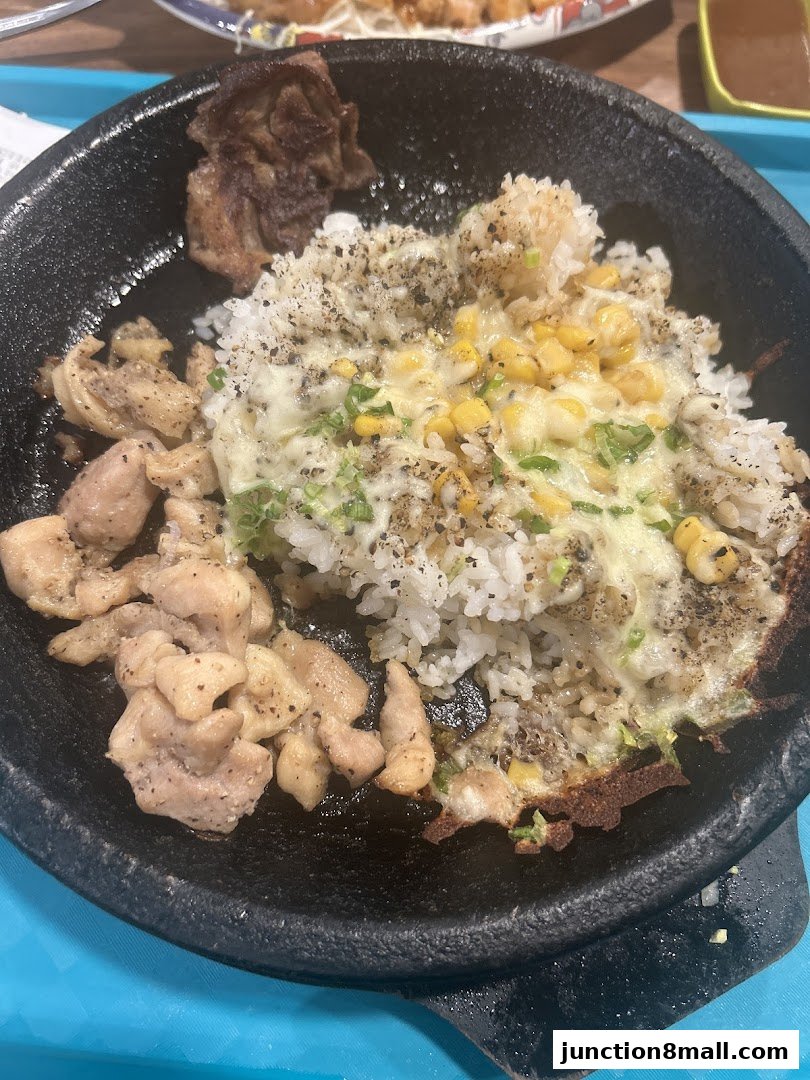 A sizzling hot plate of rice with chicken, corn, and cheese, topped with pepper.