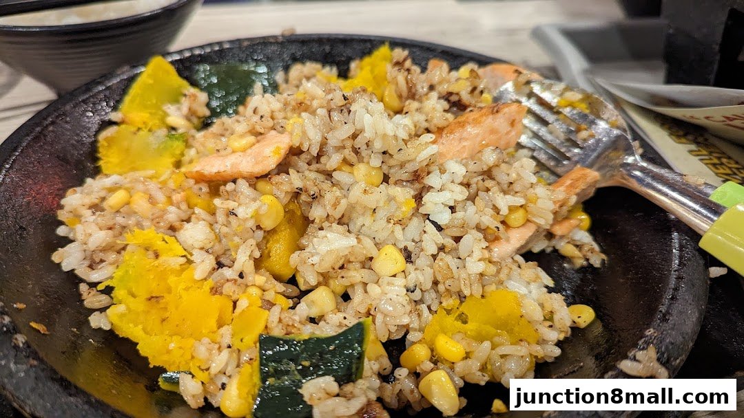 A sizzling plate of rice with salmon, pumpkin, and corn, served with a fork.