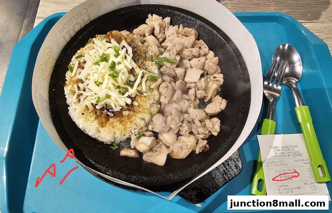 A sizzling hot plate of chicken and rice topped with cheese and spring onions, served with cutlery.