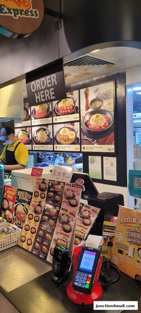 A Pepper Lunch Express counter with a menu, ordering sign, and payment terminal.