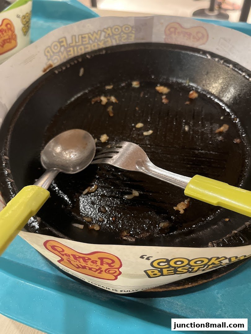 A used Pepper Lunch Express sizzling plate with cutlery on a blue tray.