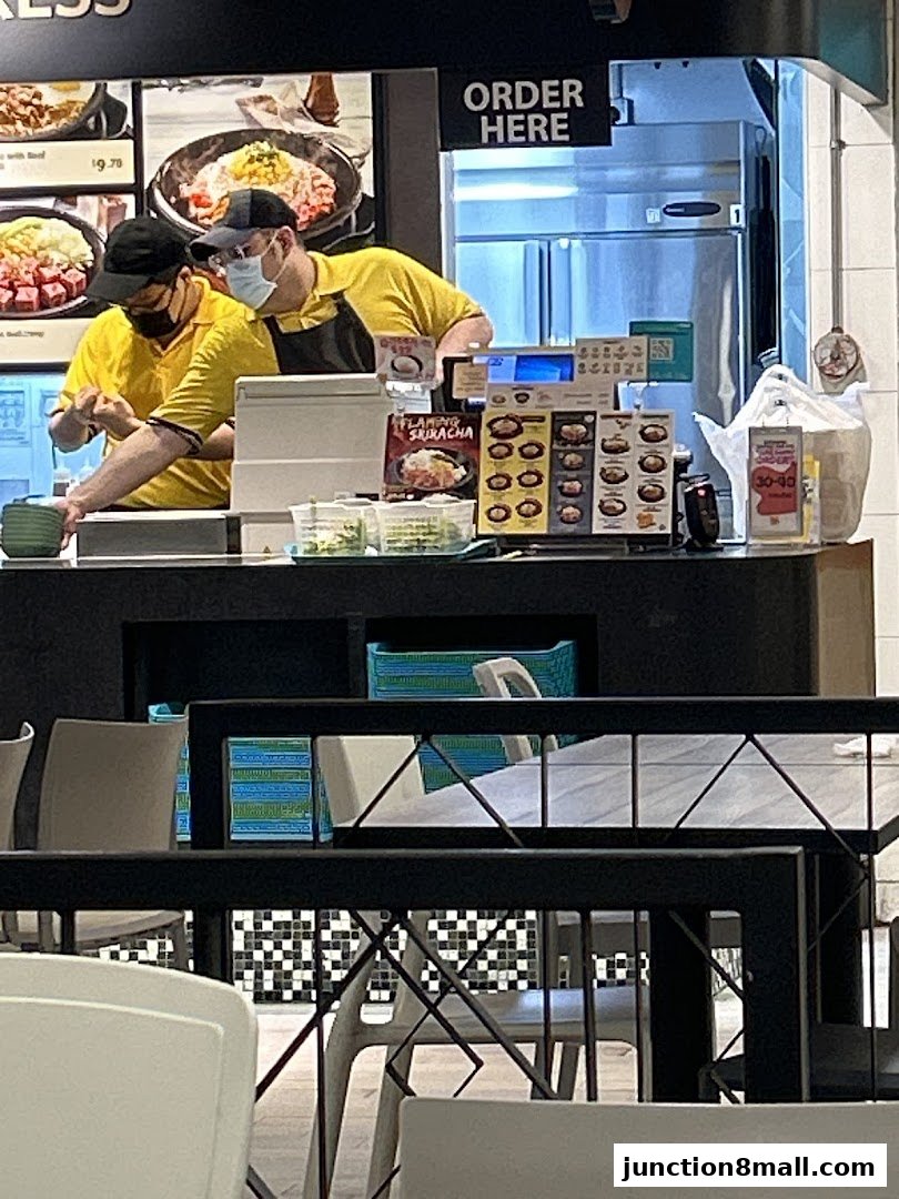 Two staff members in yellow shirts work behind a counter at Pepper Lunch Express.