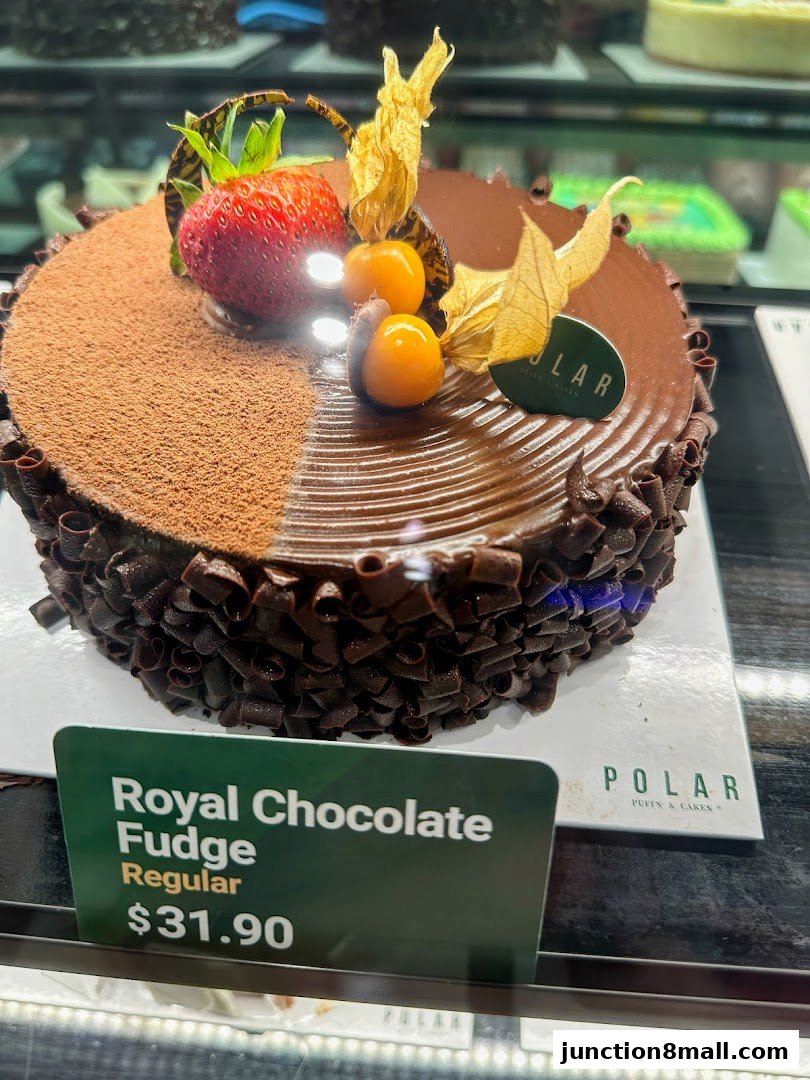 A decadent chocolate cake with fresh strawberries and physalis, displayed in a bakery.