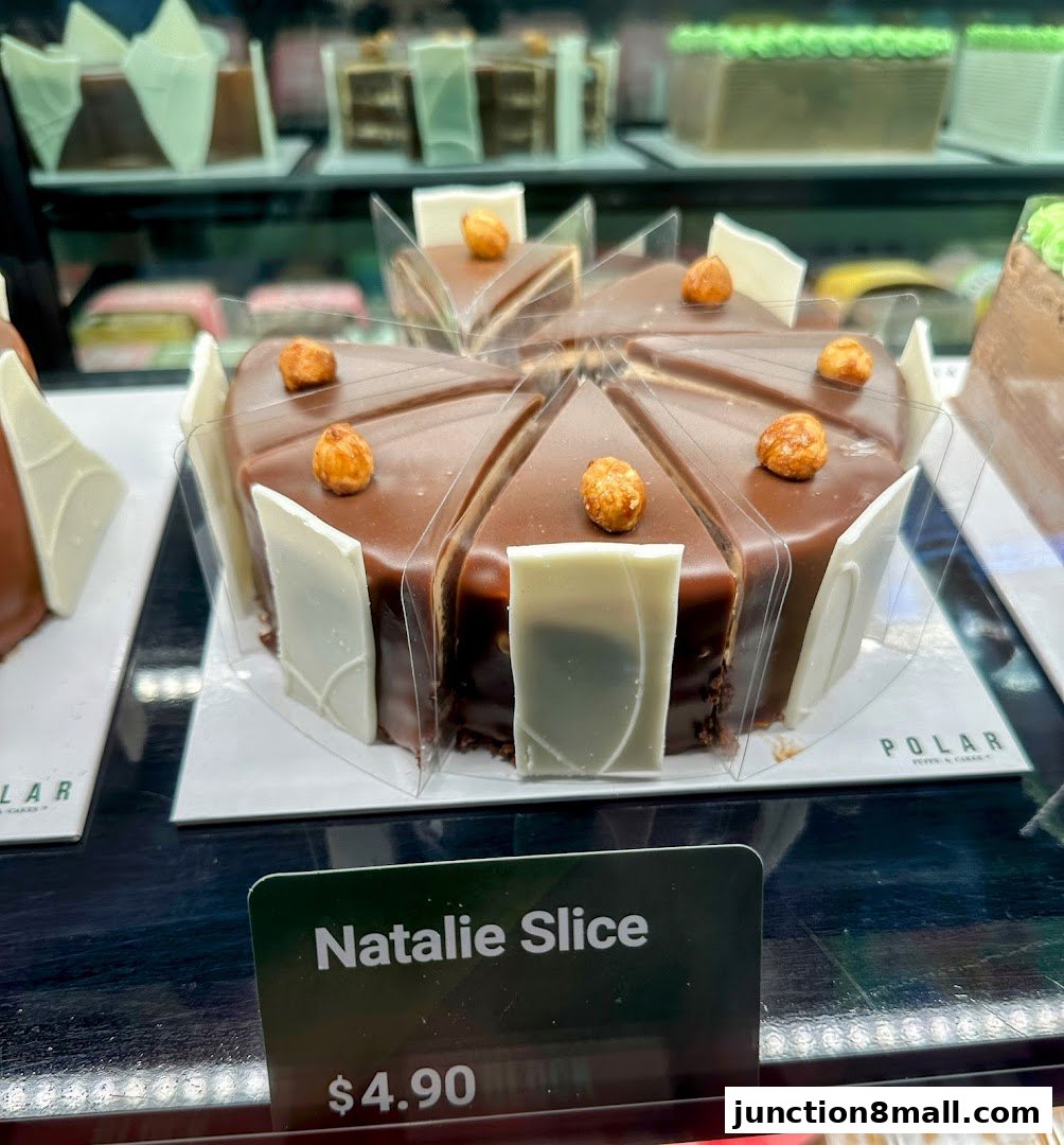 A chocolate cake slice with hazelnuts and white chocolate decorations on display.