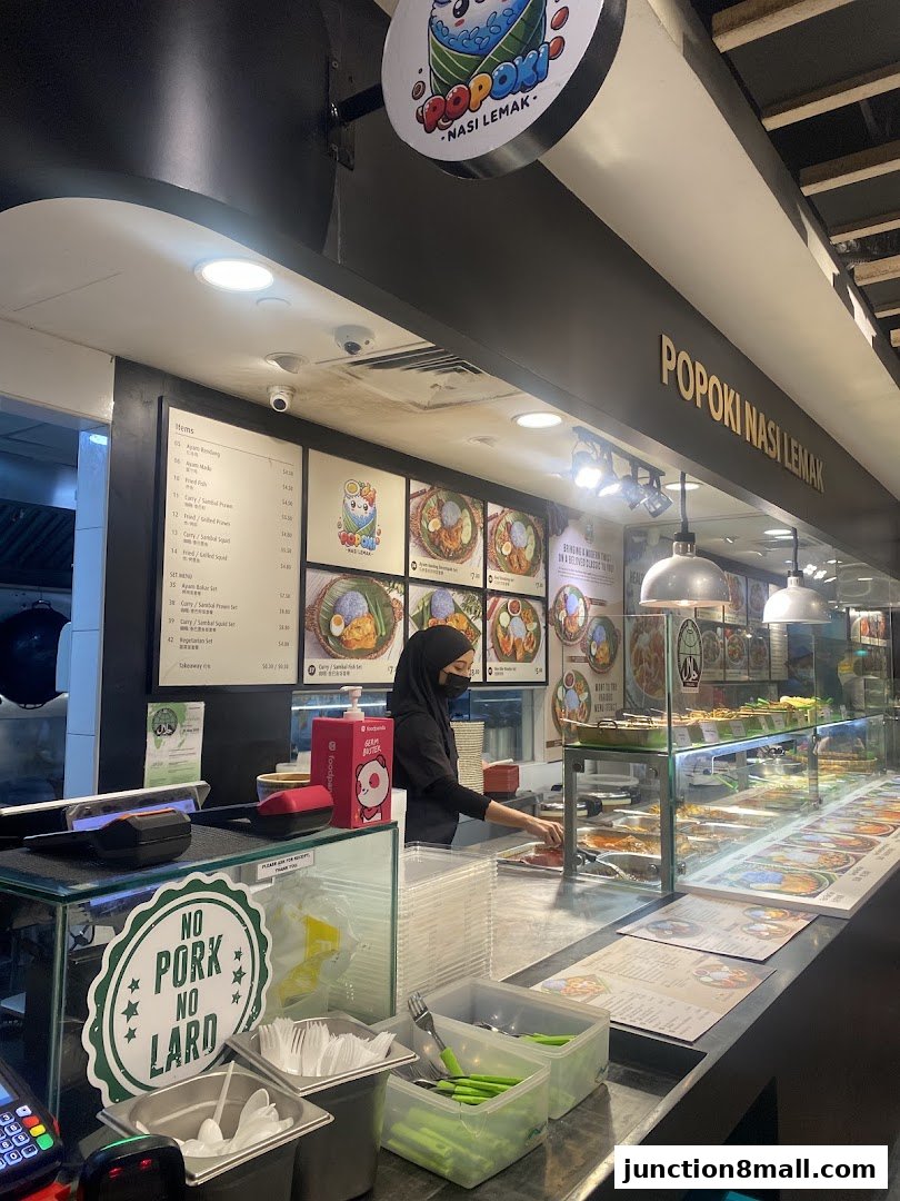 A food stall counter with a menu, food display, and staff member serving customers.