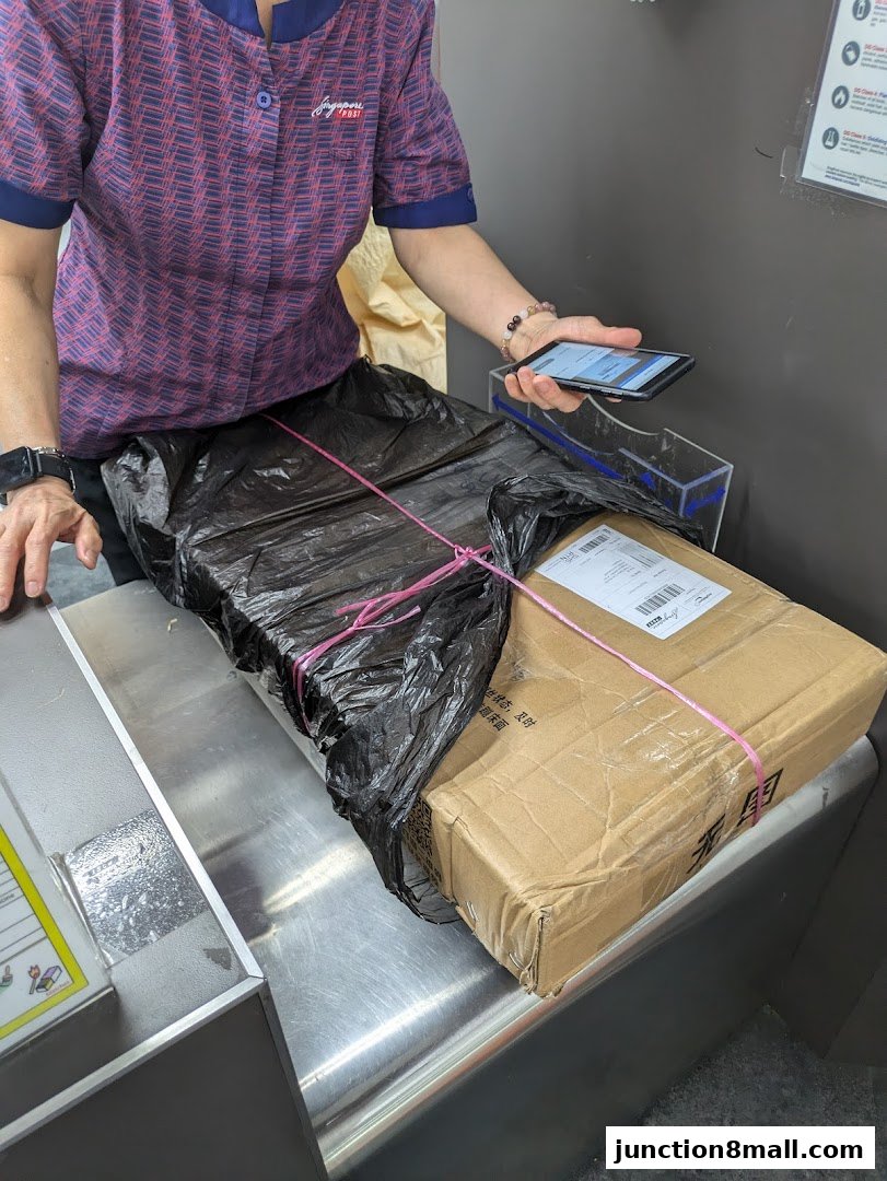 A person in a Singapore Post uniform holds a phone while packages are on a counter.