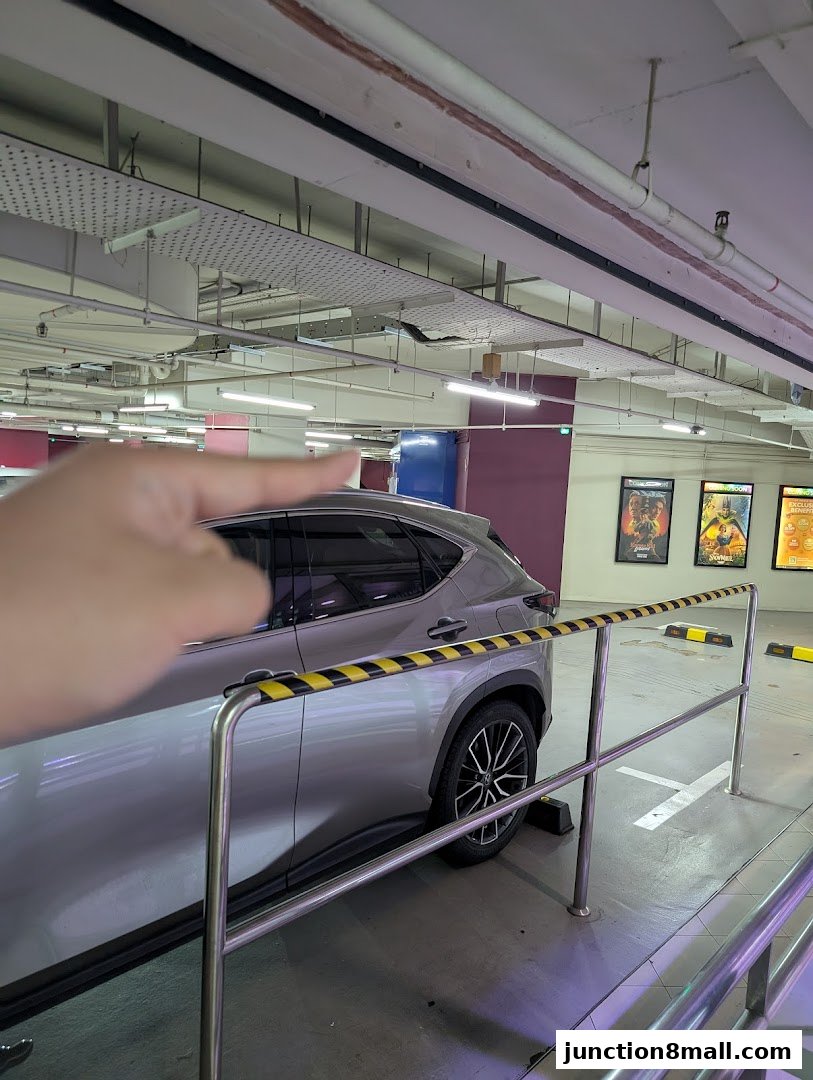 A hand points towards a silver car parked in a parking lot with movie posters in the background.