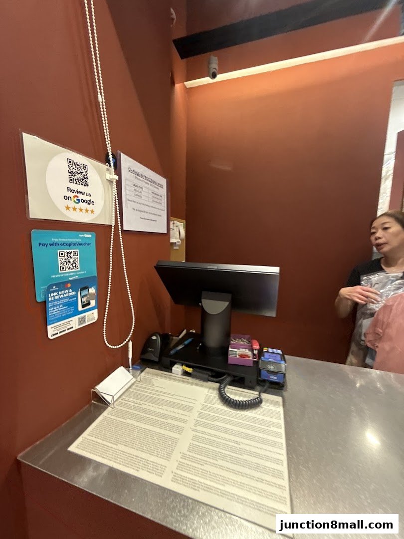 A dry cleaner's counter with a computer, payment terminal, and customer service signage.