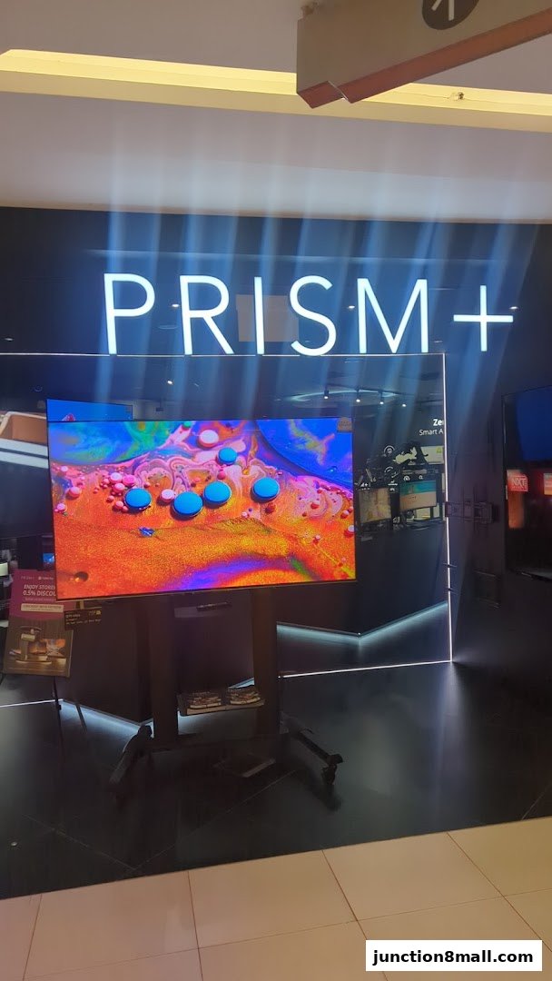 A large TV screen displays vibrant abstract art in front of the PRISM+ store.