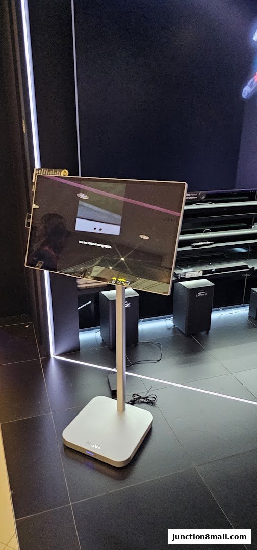 A modern display stand with a screen showing a reflection, surrounded by audio equipment.