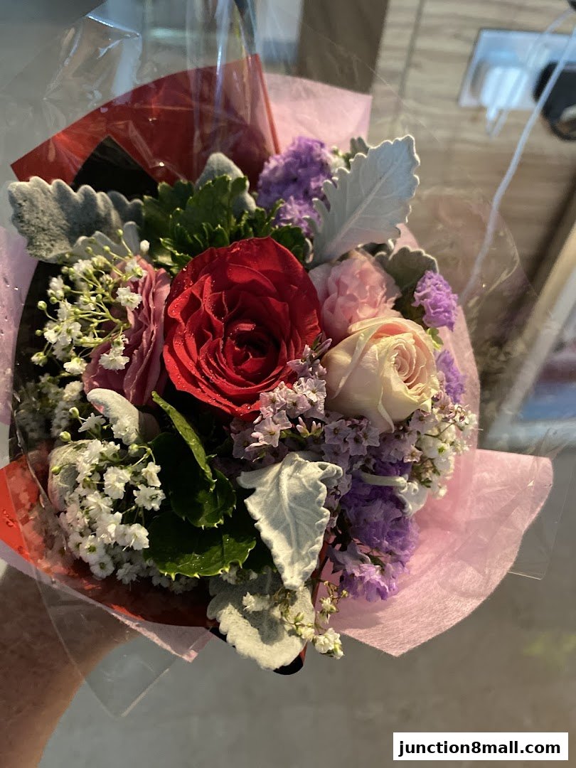 A hand holds a beautifully arranged bouquet of red, pink, and purple flowers.